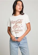 Remera color crema de corte cropped, con cuello redondo y mangas cortas. Estampado frontal con el logo de Coca-Cola, un jinete a caballo y la frase "The Wild West The Best" en color marrón.
