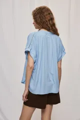 Camisa de manga corta color celeste, confeccionada en viscosa fluida, con silueta amplia y escote redondo con frunces y lazo para anudar.