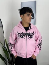 Campera con capucha y cierre frontal de cremallera, color rosado con diseño de estampado tribal negro en el pecho y las mangas.