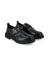 Zapatos negros de estilo masculino con textura efecto cocodrilo en la parte delantera, suela chunky dentada y tira con hebilla metálica lateral.