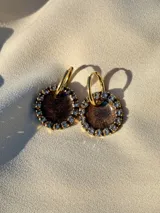 Aros colgantes dorados con dije circular de resina color turquesa, bordeado con strass. El arito es de acero quirúrgico.