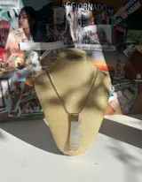 Collar con cordón fino color ocre, dije de nácar blanco con forma irregular y aplique metálico dorado.