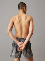 Short de baño negro con estampado de líneas onduladas blancas. Cuenta con cintura elástica ajustable con cordón, bolsillos laterales y trasero, forro de malla y logo de Calvin Klein en el bajo.