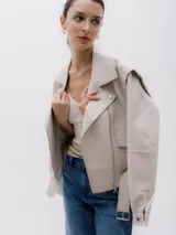 Chaqueta corta estilo biker color beige, confeccionada en piel sintética. Presenta cierre asimétrico frontal, bolsillo con cierre a la vista y bolsillo con solapa, cinturón con hebilla en la cintura.