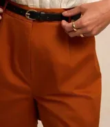 Short de vestir color beige, con cintura alta, pliegues frontales, cinturón de cuero sintético con hebilla metálica y cierre frontal con botón y cremallera.