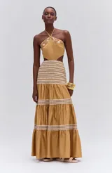 Vestido largo color mostaza, con diseño cut-out en la cintura, cuello halter con tiras para atar, y detalles bordados en el escote. La falda larga presenta paneles fruncidos con detalles tejidos en hilo crudo.