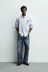 Camisa de corte regular fit confeccionada en tejido de algodón con diseño de rayas verticales. Presenta cuello abotonado, manga larga con puños abotonados, bolsillo plastrón en el pecho y cierre frontal con botones.