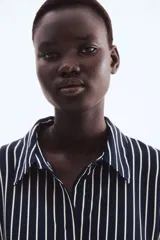 Camisa de manga larga con cuello clásico y cierre frontal de botones. Presenta un estampado de rayas verticales finas blancas sobre fondo azul marino. Los puños son anchos y también tienen rayas horizontales.