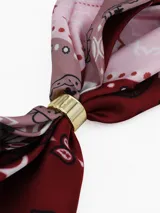 Pañuelo cuadrado de tela ligera color negro con estampado de lunares blancos y borde con franja blanca. Incluye un anillo metálico dorado para sujetar y estilizar el pañuelo.