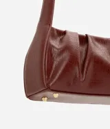 Cartera baguette de marca Satinato confeccionada en poliuretano con textura crocco en color marrón. Cuenta con diseño estructurado, cierre de cremallera y asa fija de hombro.