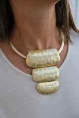 Collar rígido de metal dorado con diseño de gargantilla y tres dijes colgantes de formas rectangulares y semicirculares con acabado martillado.