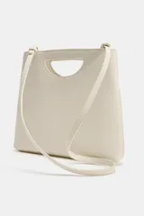 Bolso de mano de piel color rojo, con diseño de cuerpo asimétrico y asa de mano integrada con apertura lateral. Incluye correa bandolera extraíble y bolsillo interior.