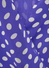 Vestido corto de poliéster con estampado de lunares, cuello en pico cruzado y diseño evasé. Presenta tirantes anchos y cierre mediante lazo lateral.