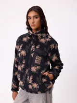 Campera reversible de diseño holgado, con un lado en tejido sherpa estampado con motivos florales en tonos negro y beige, y el otro lado en nylon negro. Cuenta con cierre frontal y cordones ajustables en el ruedo.