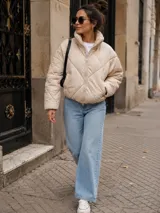 Campera puffer color beige claro, con diseño acolchado de rombos, cuello alto y cierre frontal completo.