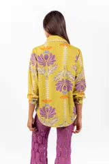 Camisa de manga larga con cuello clásico y cierre frontal de botones, confeccionada en tejido de color verde lima con estampa floral en tonos morados y naranjas.