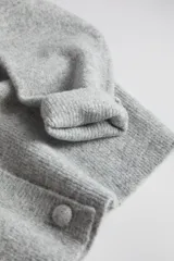 Cardigan de punto gris claro, con escote en V profundo, cierre frontal cruzado con botones y mangas largas holgadas.