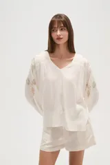 Blusa holgada color blanco roto, con escote en V y mangas largas abullonadas con bordados florales en tono dorado/marrón claro en los hombros y mangas.