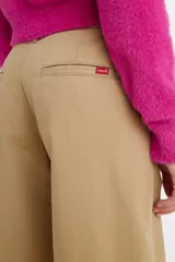 Pantalón de corte baggy en color beige, con diseño de tiro medio y pernera ancha. Presenta cierre frontal con botón y cremallera, y bolsillos laterales.