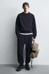 Mochila negra lisa con acabado engomado, compartimento principal con cierre de cremallera, bolsillo interior con cierre, bolsillo frontal con cierre, parte posterior acolchada con banda de sujeción para equipaje, asa de mano y dos asas de hombro ajustables y acolchadas.