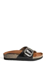 Sandalia plana tipo birkenstock con tira ancha de cuero negro, gran hebilla metálica ajustable y suela de corcho con base de goma.