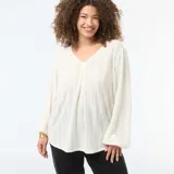 Blusa de punto calado en color blanco, con cuello en V y mangas largas con puños holgados. Presenta un diseño de rayas verticales sutiles y un pliegue central en el frente.