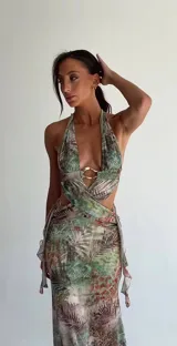 Vestido largo estampado con diseño tropical, escote halter profundo y detalle de argolla metálica en el centro del busto. Presenta aberturas laterales en la cintura y falda con caída fluida.