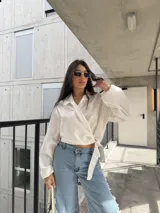 Camisa cruzada de color blanco, manga larga con puños amplios y lazo para atar en la cintura.