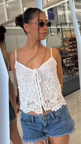 Top blanco de tirantes finos y escote en V, con delicados bordados florales y detalle de lazo frontal. El ruedo presenta un diseño de encaje festoneado.
