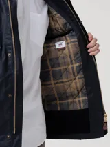Chaqueta de hombre color azul marino, confeccionada en tela encerada impermeable y cortaviento. Cuenta con cuello de cotelé, cierre frontal con broches y cremallera, y múltiples bolsillos exteriores e interiores. El interior está forrado en franela y tiene relleno de THERMORE, hecho de fibras recicladas.