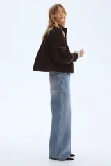 Campera corta de sarga color marrón oscuro, con cuello alto, cierre frontal con botones y bolsillos laterales. Presenta mangas largas abullonadas con fruncidos en los hombros y puños ajustados.