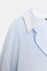 Camisa oversize de algodón con estampado de rayas finas, cuello solapa, escote en pico y manga larga con puños abotonados. Presenta un diseño con pliegues laterales y cierre frontal con botones.