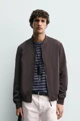 Cazadora bomber ligera de tejido técnico color verde oliva, con cuello, puños y bajo en rib elástico. Presenta cierre frontal de cremallera y bolsillos de vivo en la cadera.