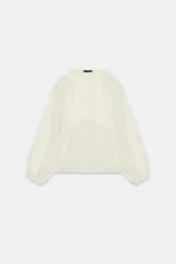 Blusa blanca de manga larga y escote en V, con detalles de crochet en el pecho y puños.