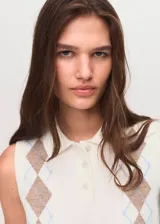 Chaleco de punto fino sin mangas, con cuello polo y cierre frontal de botones. Presenta un diseño de rombos en tonos neutros sobre una base color crema.