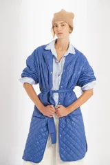 Campera azul capitoneada de nylon con forro de algodón y relleno de poliéster. Tiene ruedo curvo, largo midi, cinta para atar a la cintura y bolsillos delanteros.