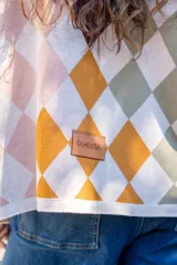 Sweater tejido de algodón con diseño de rombos multicolor en tonos marrones, azul y rojo. Presenta una silueta oversize, cuello redondo y mangas largas abullonadas con puños ajustados.