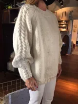 Sweater amplio de lana merino tejido a mano, color beige, con cuello redondo y mangas largas con diseño de trenzas.