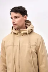 Campera tipo parka de gabardina color beige, con capucha ajustable, cierre frontal y bolsillos laterales con solapa. Presenta un diseño clásico con interior capitoneado.