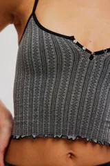 Top corto sin costuras de tejido acanalado y texturado color marfil, con escote redondo amplio, botonadura henley al frente con pequeños botones a presión, tiras finas fijas y terminación con ruedo en lechuga, de calce ajustado.
