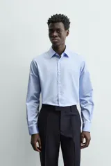 Camisa de manga larga, color blanco, con cuello italiano y corte slim fit. Presenta cierre frontal de botonadura y puños con botón.