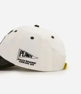 Gorra de béisbol de seis paneles, color blanco con visera curva en contraste de color verde militar. Presenta un bordado frontal de Snoopy junto a un banderín y el número cinco, y un bordado lateral con el texto 'Peanuts Athletic Department'.