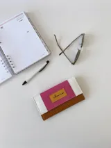 Billetera de cuero con diseño tricolor que combina texturas: cuerpo principal en marrón con textura tipo lagarto, solapa central en fucsia con textura granulada y detalles en blanco con textura tipo cocodrilo. Incluye una etiqueta central de cuero en color tostado con la marca grabada y cierre con broche.