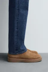 Bota estilo Chelsea de hombre, confeccionada en piel con acabado de serraje en color tostado. Presenta elásticos laterales a tono, horma redonda y suela plana del mismo color.