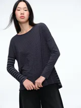 Camiseta de manga larga con cuello redondo y diseño a rayas horizontales en tonos gris y negro. Presenta un corte holgado y cómodo con caída fluida.