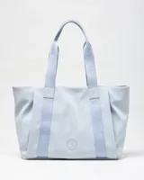 Cartera tipo tote color celeste, con asas de hombro y tiras frontales con la inscripción de la marca en relieve. Cuenta con un pequeño aplique circular con el logo en el centro.