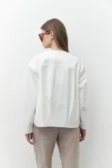 Chaqueta bomber blanca con cierre frontal, mangas largas con diseño geométrico calado en los hombros y puños elásticos.