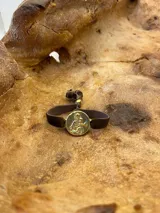 Pulsera con dije redondo dorado con diseño abstracto y cinta de terciopelo elástico color gris claro.