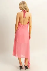 Vestido midi de color rosado con escote halter y espalda descubierta. Presenta un diseño asimétrico en el ruedo y un detalle de flor aplicada en la cintura.