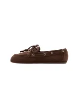 Zapato mocasín de gamuza marrón, estilo náutico, con detalles de cordones con nudo en el empeine, ojales metálicos plateados en los laterales y suela plana.